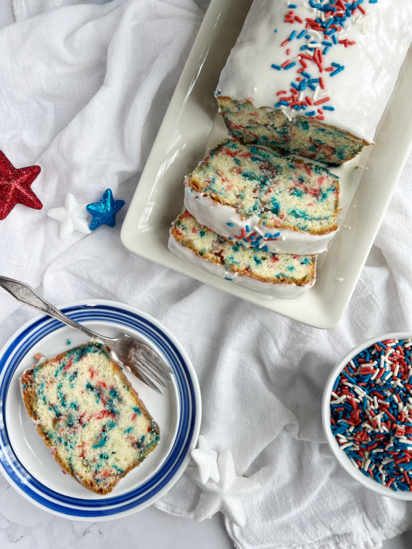4th of July sprinkles pound cake sliced with a white bowl of red, white and blue sprinkles