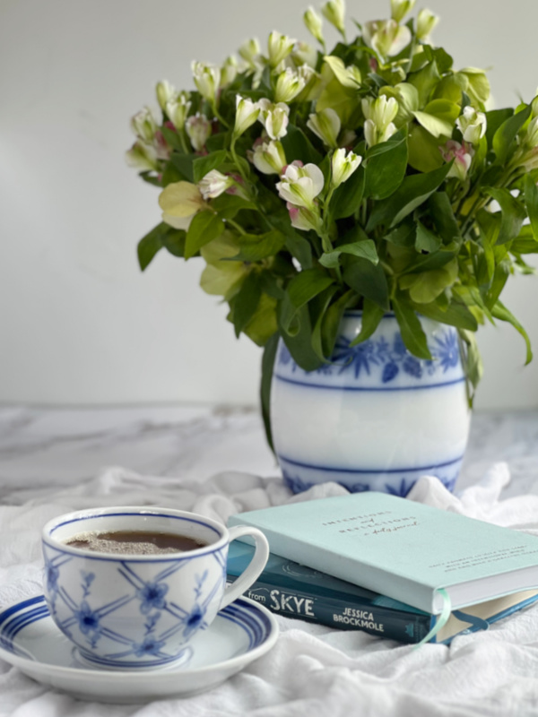 100 Ways to Have a Cozy Winter Reset, Cup of tea in a blue and white cup, a journal, a book and blue and white vase of flowers.
