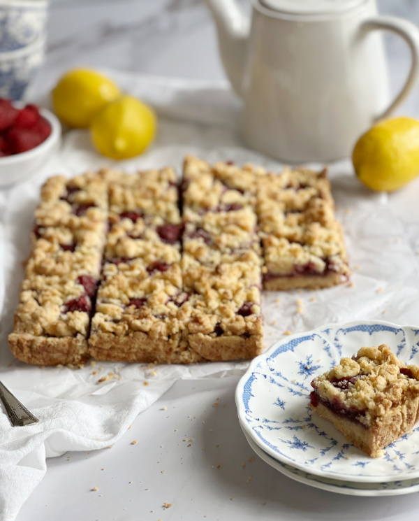Lemon Raspberry Crumble bars on a plate with lemons and raspberries in a bowl.