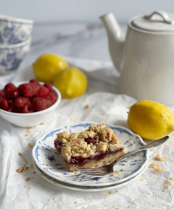 Lemon raspberry bar on a blue and white plate with scattered lemons and a white teapot.