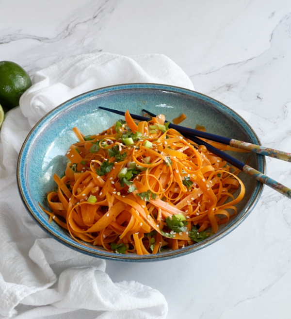 Raw Carrot Salad (5 Minute Viral Tik Tok Recipe) in a blue pottery bowl with limes and chop sticks. 