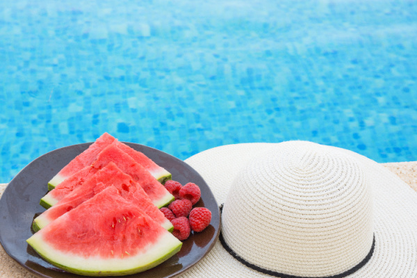watermelon and raspberries on a black plate and a hat on the side of the pool.
