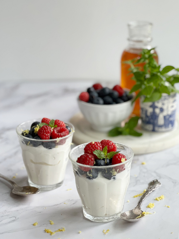 whipped yogurt cream with summer berries and honey and a blue and white vase with greens.