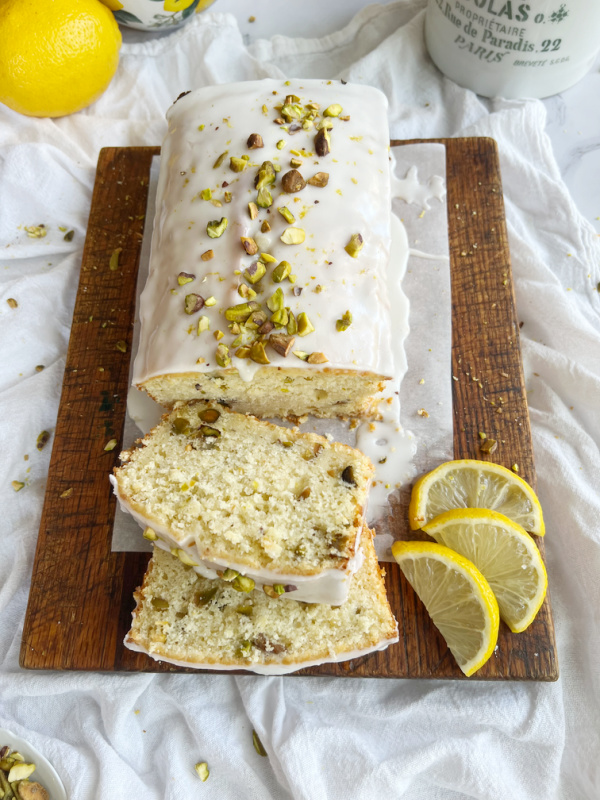 lemon pistachio breakfast bread sliced on a board with 3 lemon slices.