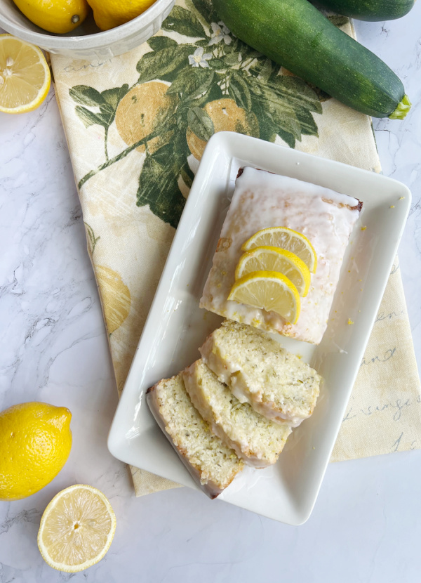 lemon zucchini bread on a white platter with lemons and zucchini.