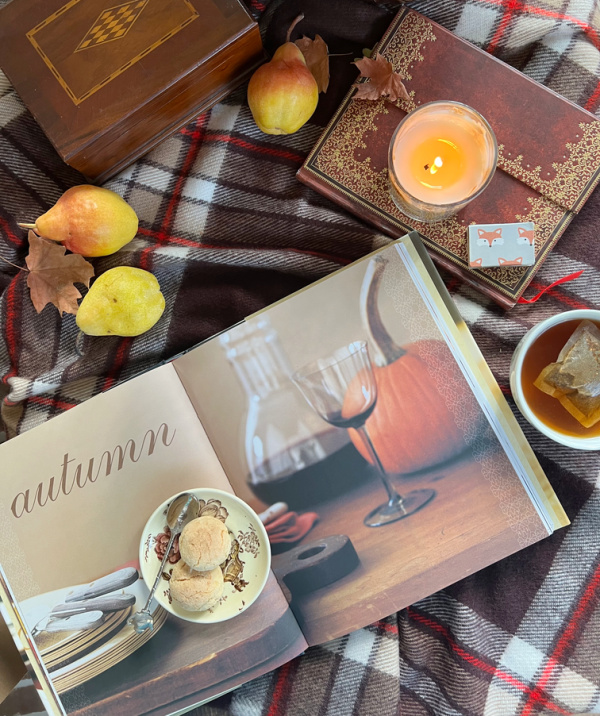 Autumn flatlay with a book open to a page that says Autumn sitting on a bad blanket with a cup of tea and some pears.