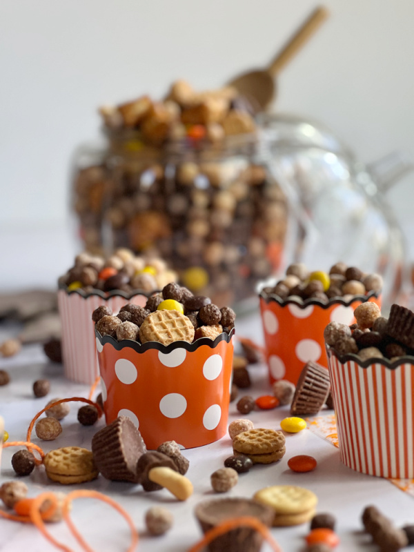 Peanut Butter Fall Snack mix in a pumpkin and scattered with orange twine and orange and white paper cup with dots.