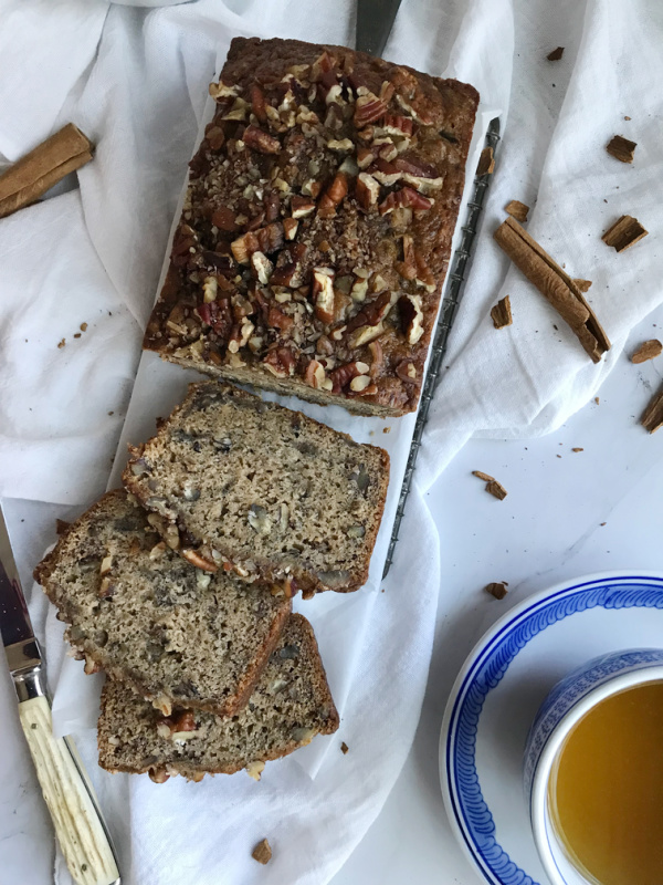 spiced banana bread sliced with a horn knife and blue and white cup of tea.