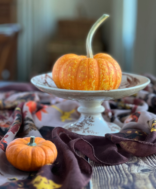 Orange pumpkin on a brown and white transfer ware stand.
