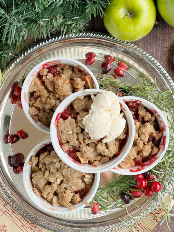 Cranberry apple crisp with vanilla ice cream in white ramekins on a silver plate.