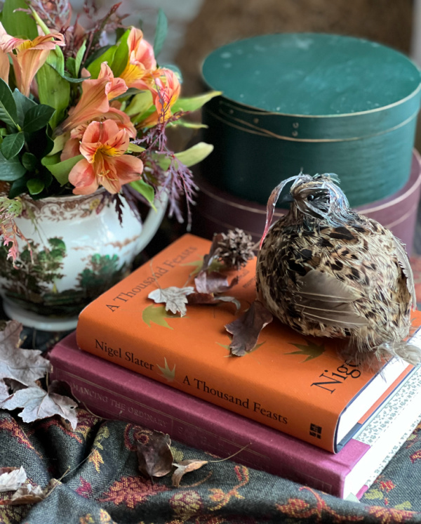 Fall books and a faux quail with a pitcher of orange flowers.
