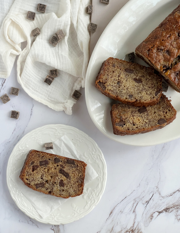 Crystallized Ginger Chocolate Banana Bread sliced on a plate and a platter with scattered chocolate.